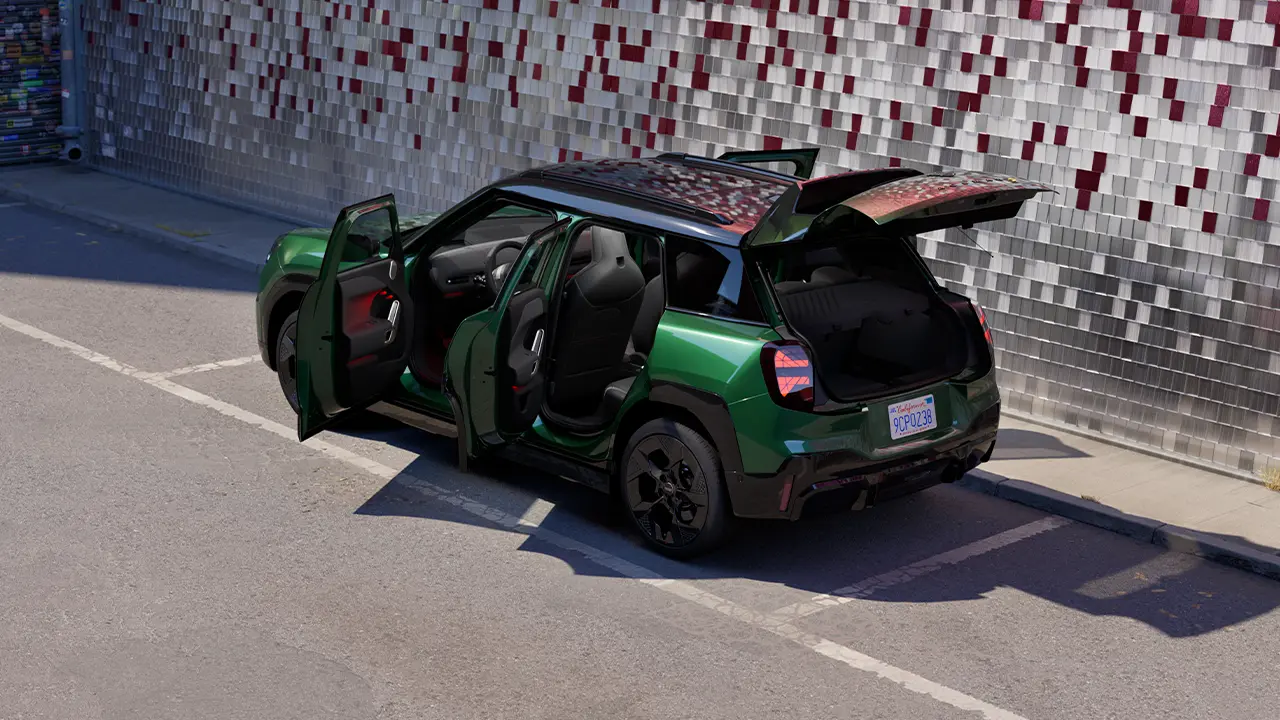 Заден страничен изглед на паркирано изцяло електрическо MINI Aceman в цвят British Racing Green с отворени всички врати и цветна стена на заден план