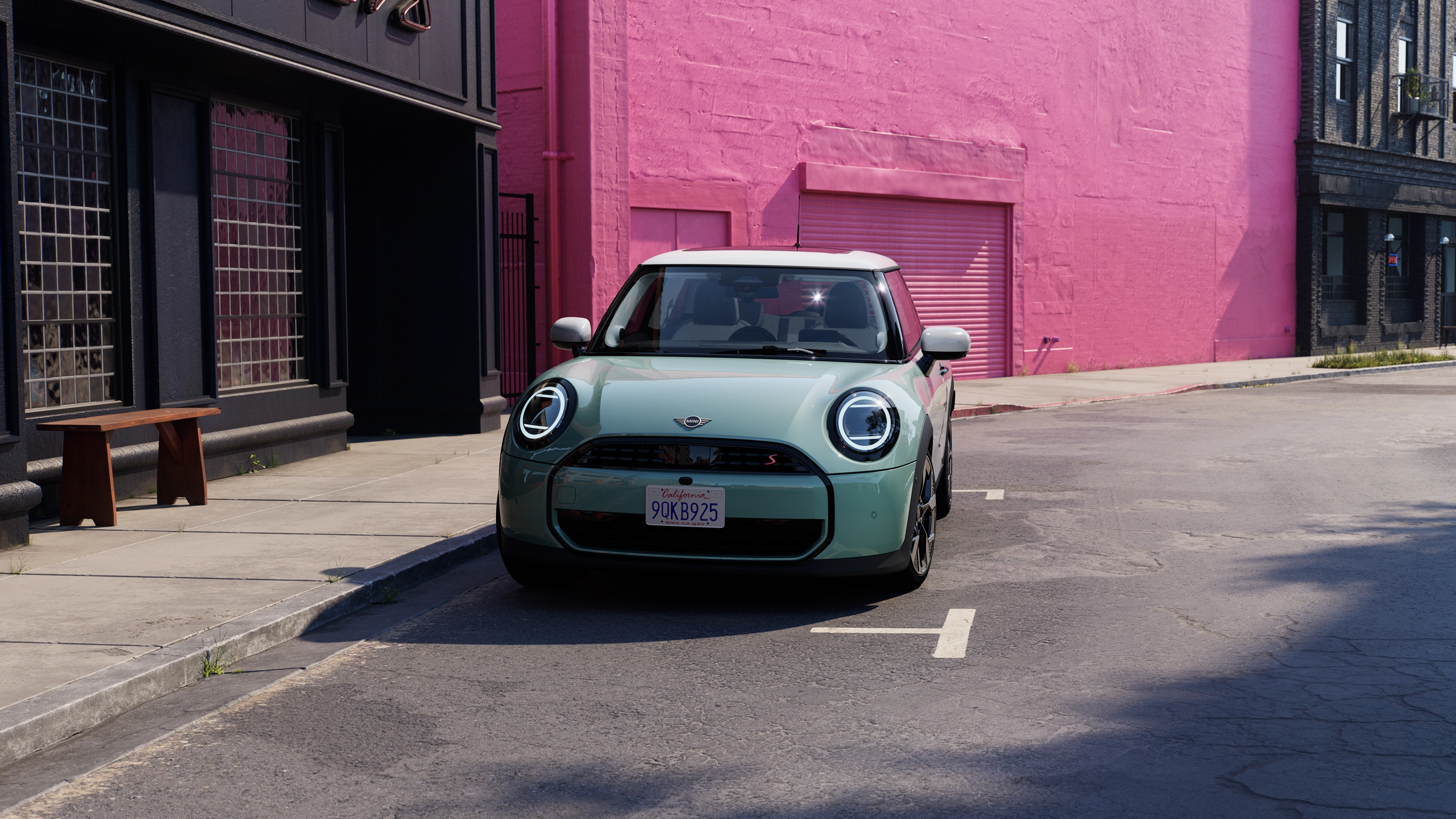 Изглед отпред на паркиращо MINI Cooper в цвят Ocean Wave Green с бял покрив на улицата с розова стена на фон