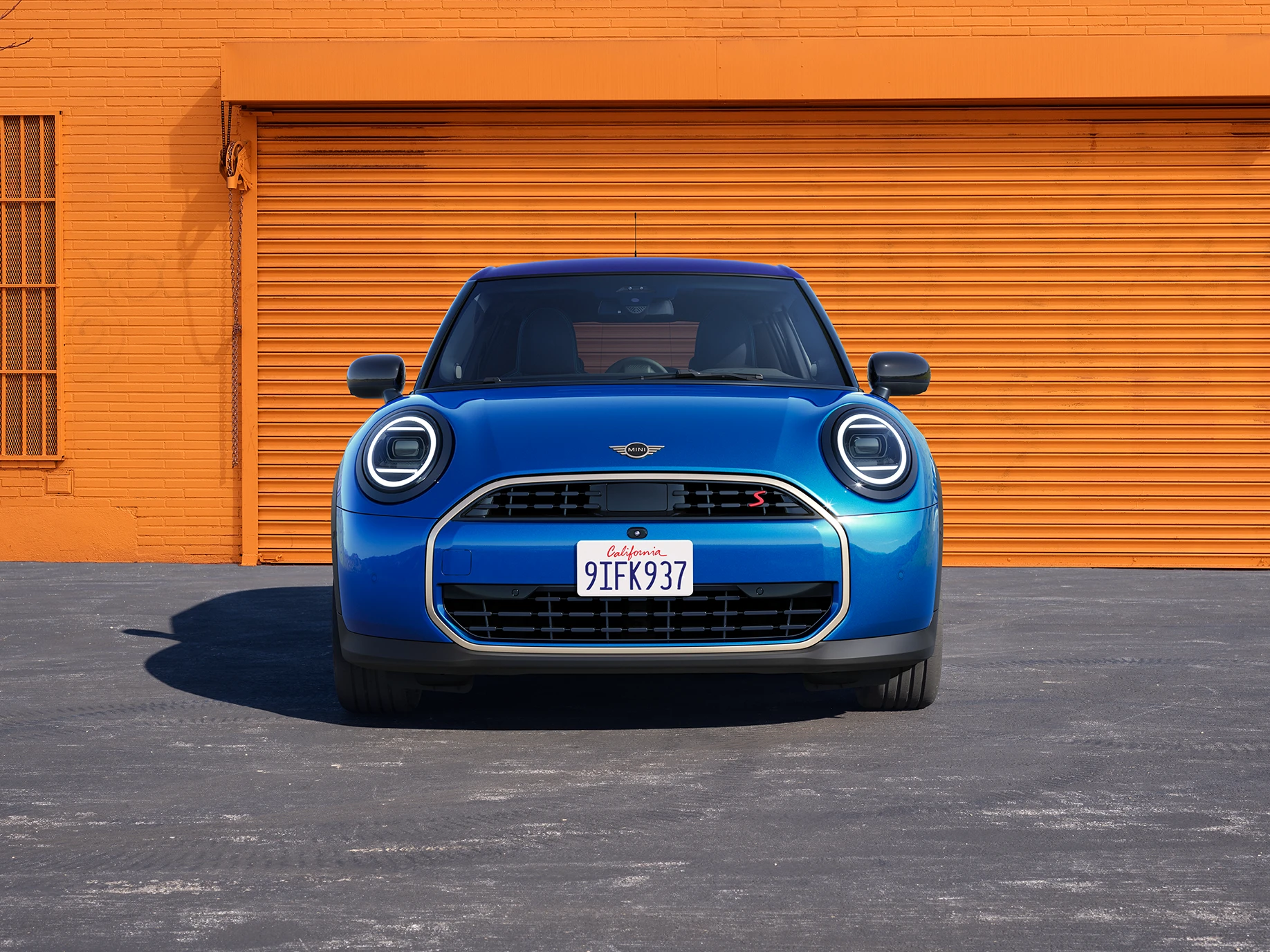 Изглед отпред на MINI Cooper 5 врати в Icy Sunshine Blue и многоцветен покрив в синьо.