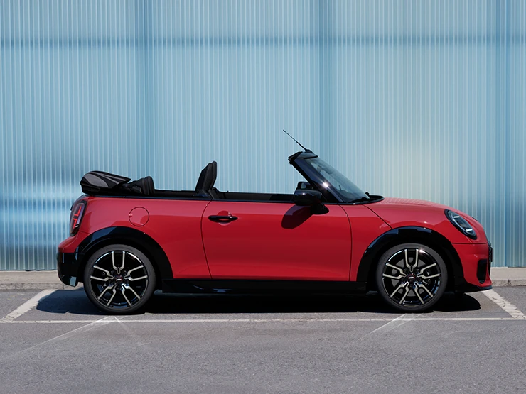 Страничен изглед към MINI Cooper Cabrio в цвят Chili Red на улица.