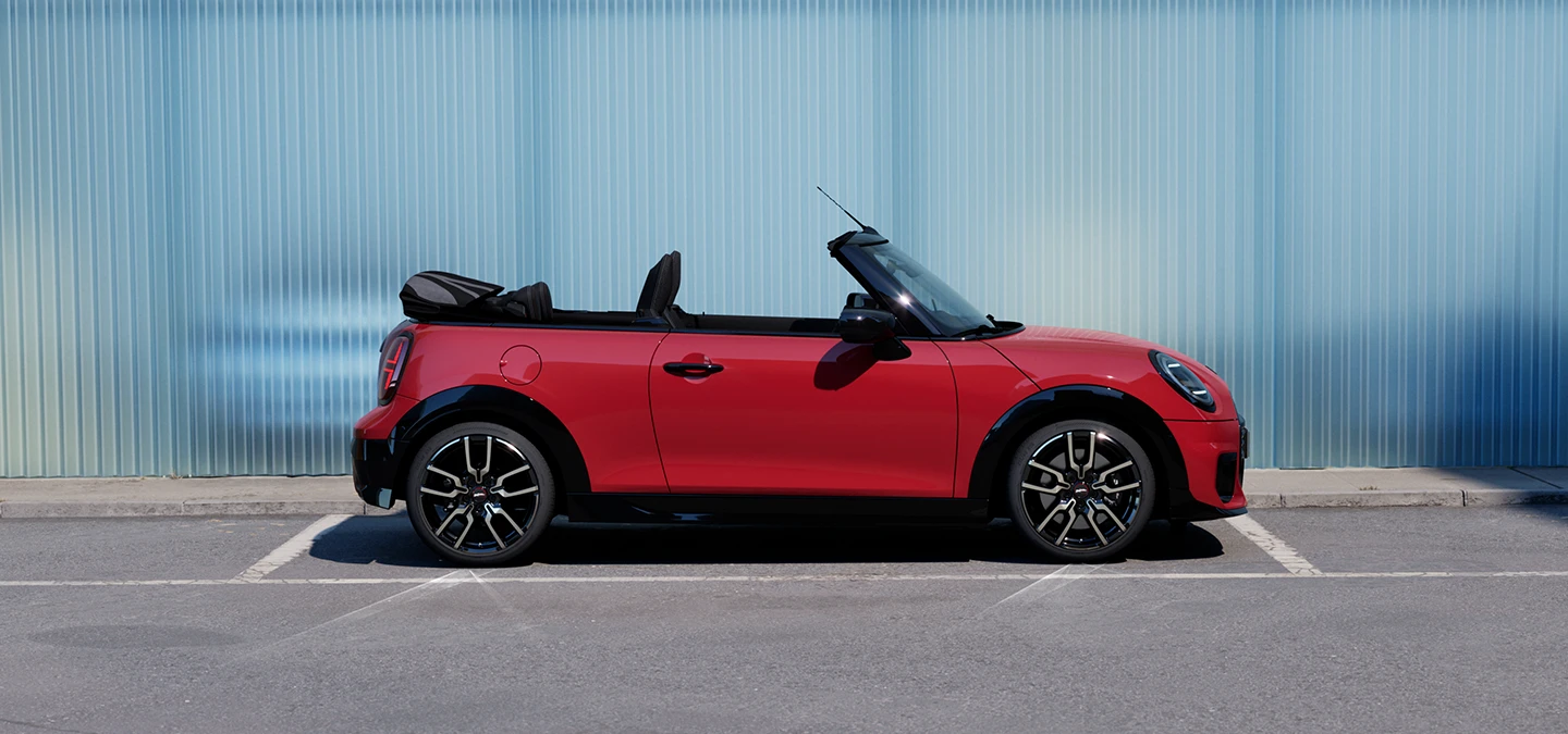 Страничен изглед към MINI Cooper Cabrio в цвят Chili Red на улица.