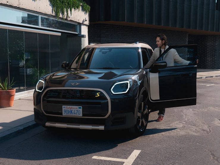 Изглед отпред на напълно електрическото MINI Countryman в цвят Midnight Black с покрив в цвят Vibrant Silver на улица.