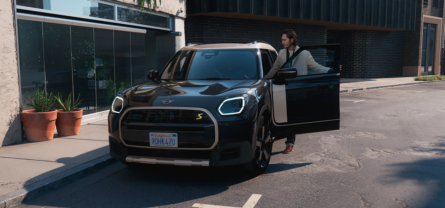 Изглед отпред на напълно електрическото MINI Countryman в цвят Midnight Black с покрив в цвят Vibrant Silver на улица.