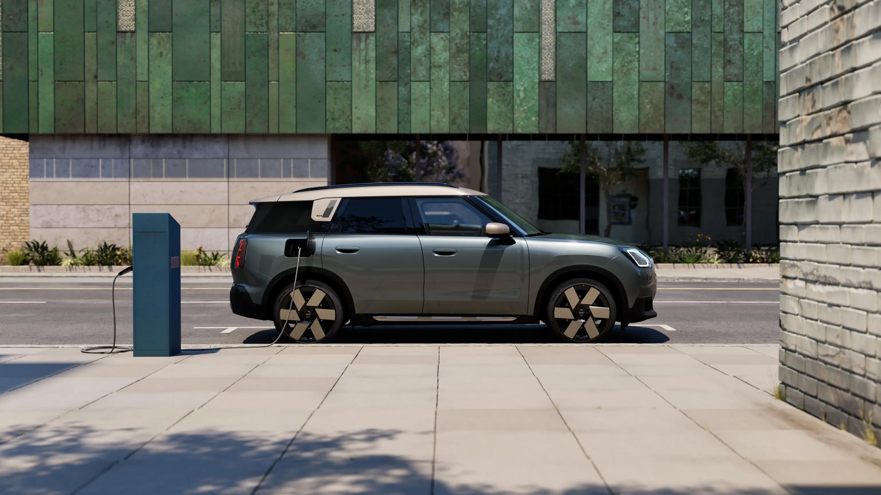 Страничен изглед на зареждащо се напълно електрическо MINI Countryman в цвят Smokey Green с покрив в цвят Vibrant Silver на улицата