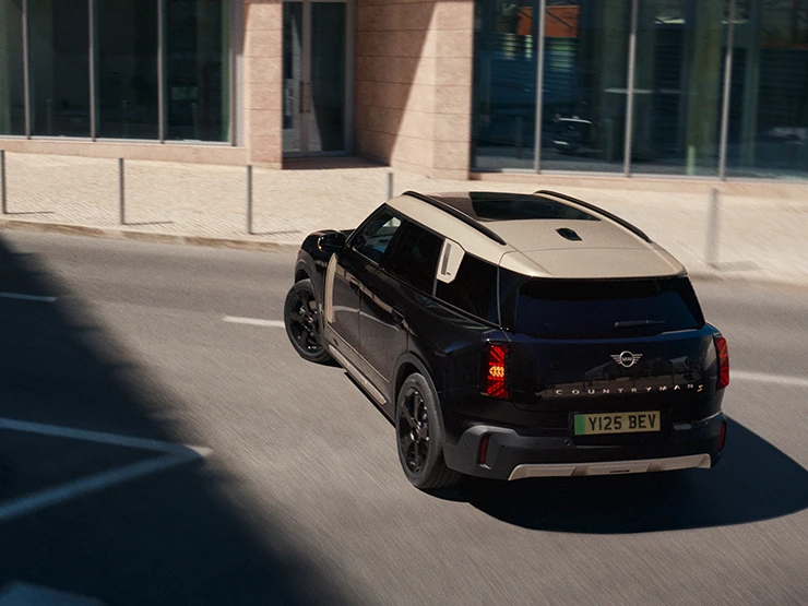 Изглед отзад и отгоре на напълно електрическото MINI Countryman в цвят Midnight Black с покрив в цвят Vibrant Silver, което паркира.