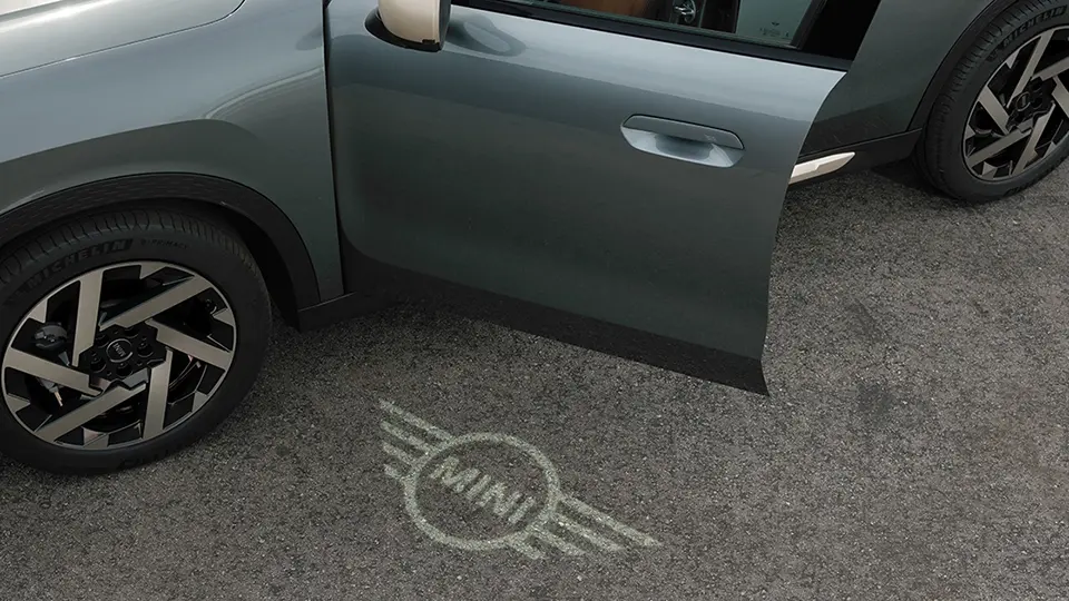 Външен изглед на MINI Countryman с отворена врата и приветствена светлина с логото на MINI на земята