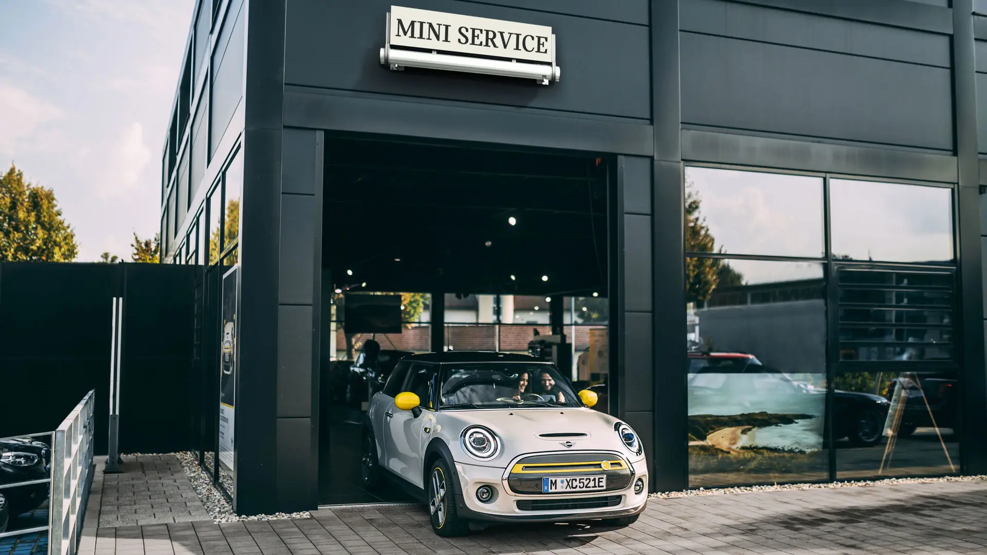 Помещение на MINI Сервизен партньор с клиентка, която изкарва новото си MINI Electric на предната площадка