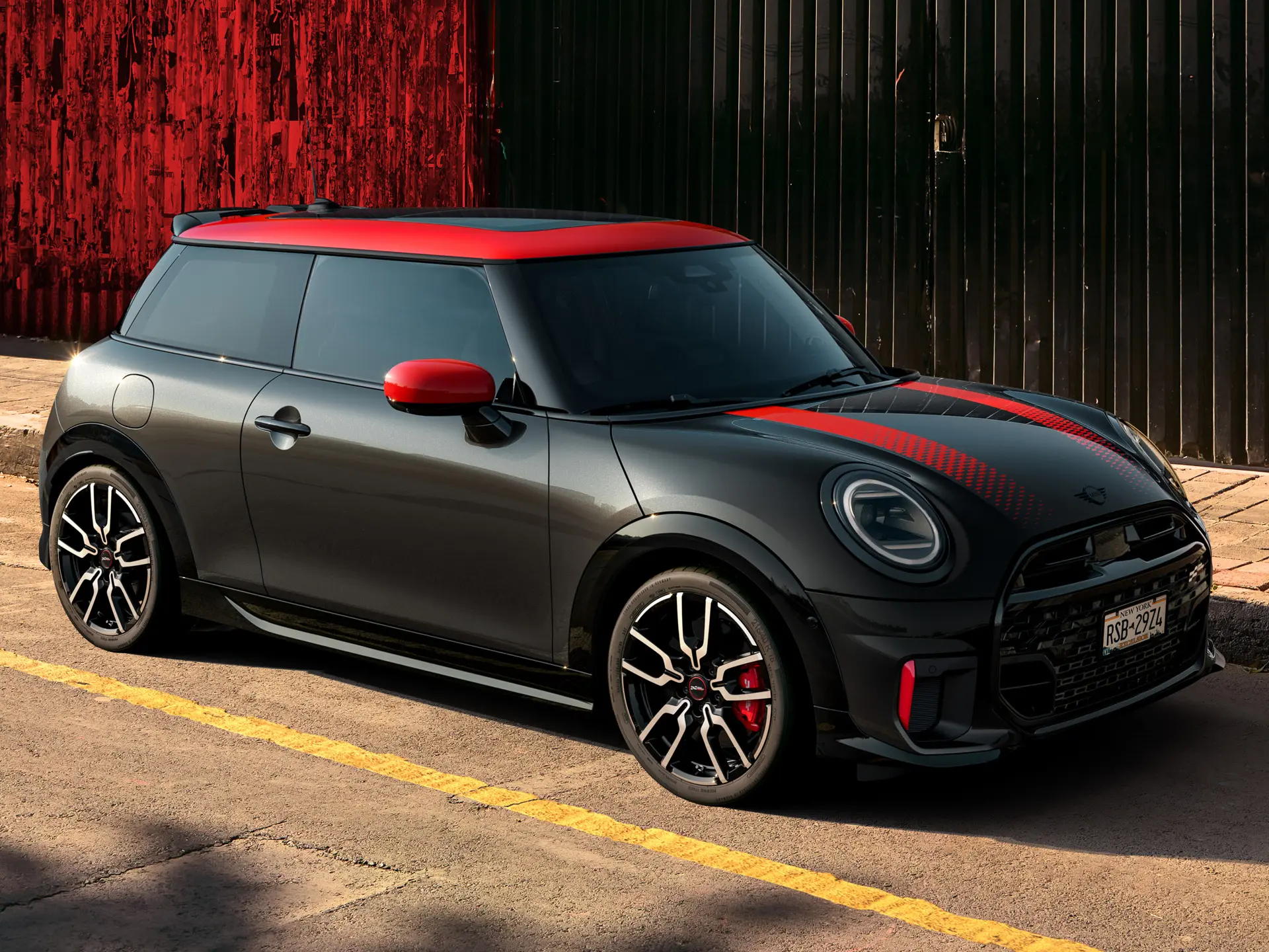 MINI John Cooper Works с 3 врати в цвят Midnight Black с покрив и корпуси на външните огледала в цвят Chilli Red и червени спортни ленти, страничен изглед, паркиран на улицата.