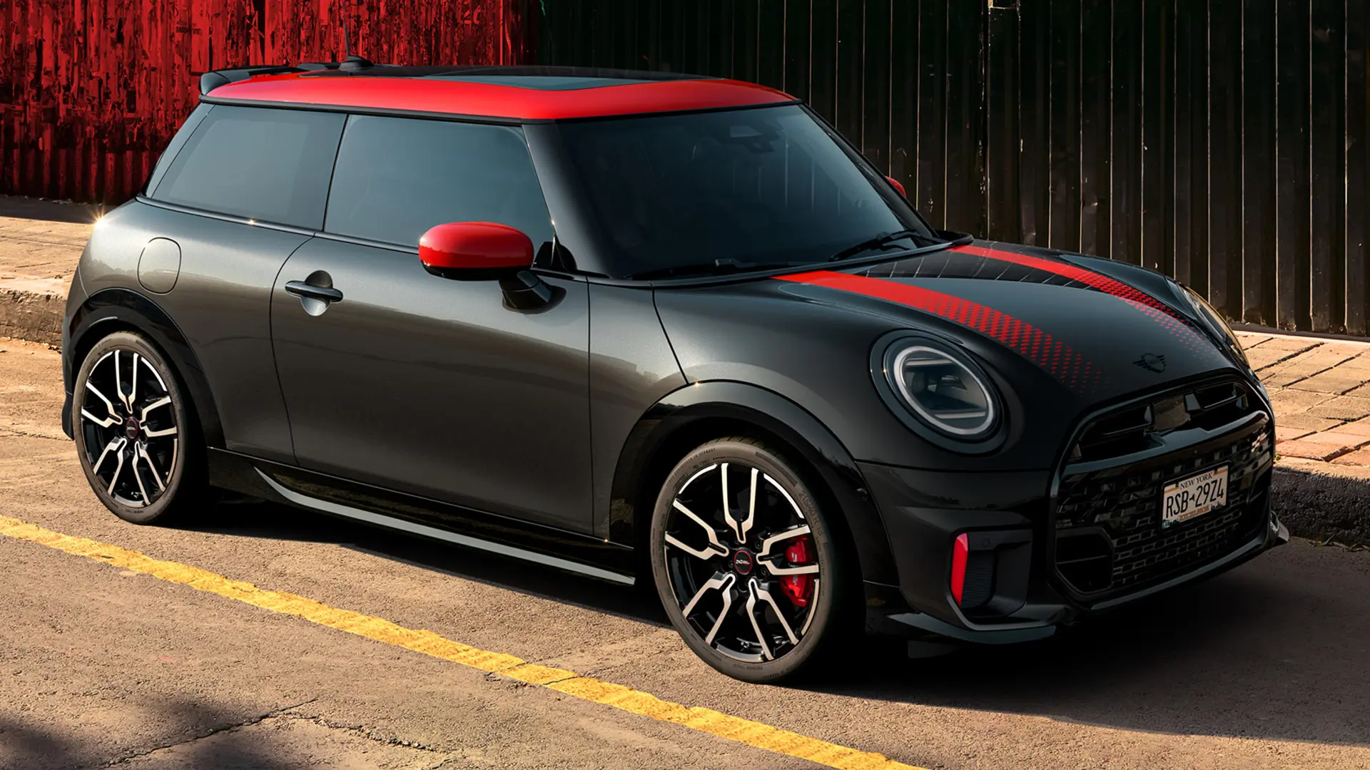 MINI John Cooper Works с 3 врати в цвят Midnight Black с покрив и корпуси на външните огледала в цвят Chilli Red и червени спортни ленти, страничен изглед, паркиран на улицата.