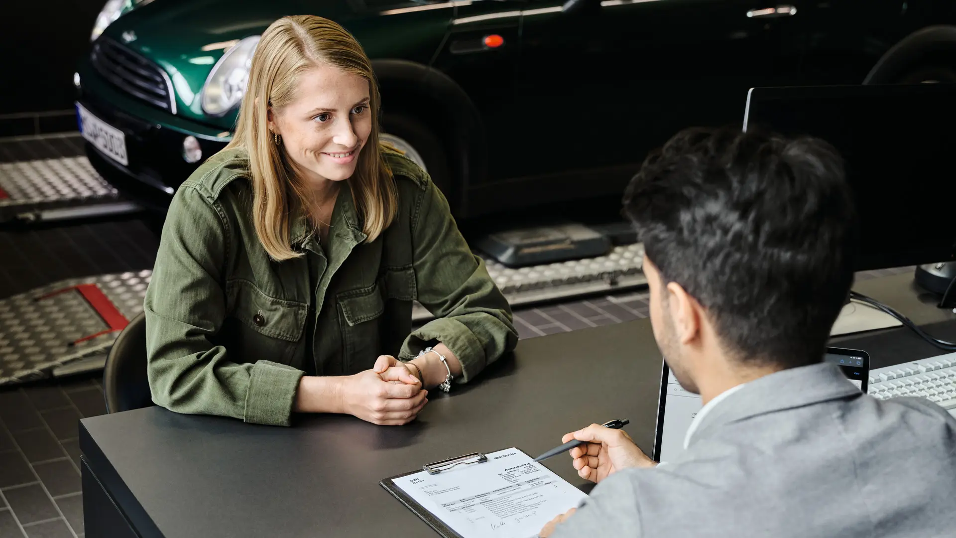 Център на MINI с консултант, който съветва клиент относно опциите за обслужване, като и двамата седят на маса.