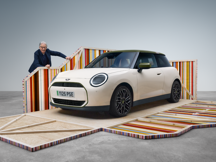 Преден страничен изглед на изцяло електрическото MINI Cooper Paul Smith Edition в Inspired White с дизайнер Пол Смит