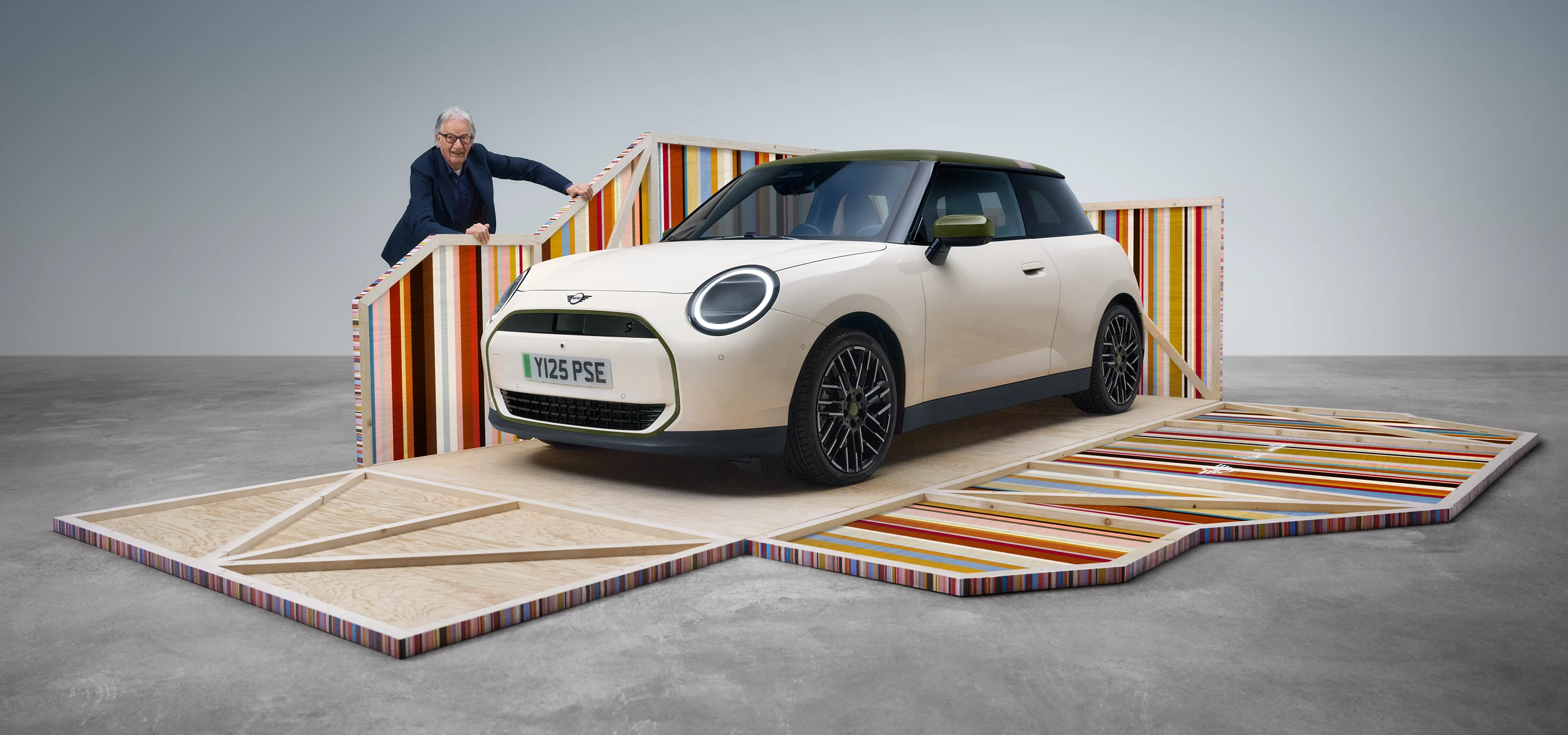 Преден страничен изглед на изцяло електрическото MINI Cooper Paul Smith Edition в Inspired White с дизайнер Пол Смит